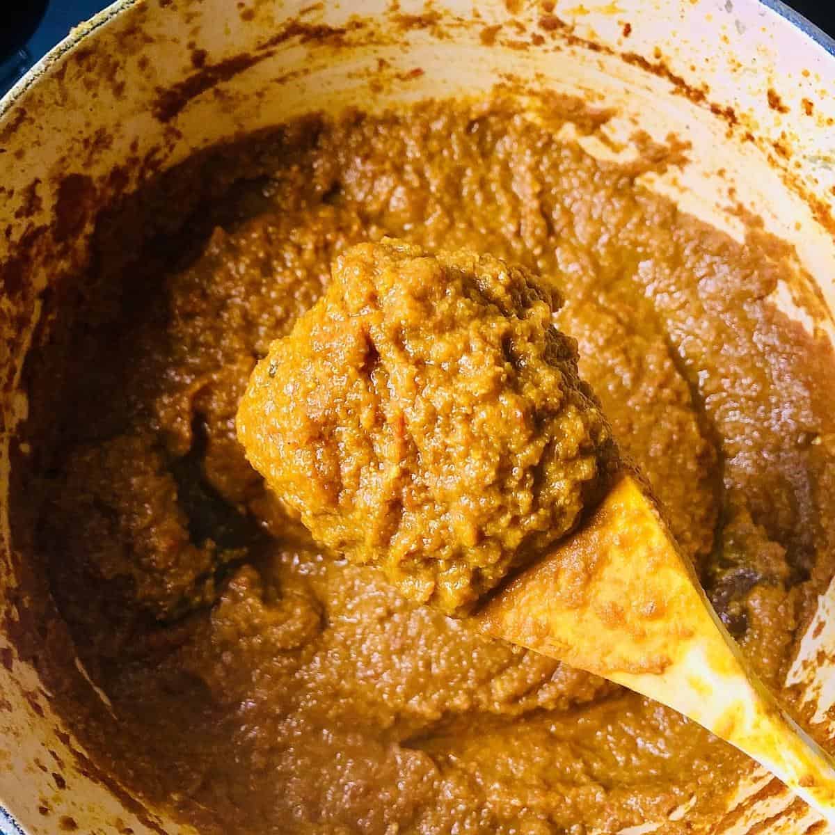 Indian gravy cube mix on a wooden spoon held over a pot containing the gravy cube mix after final cooking