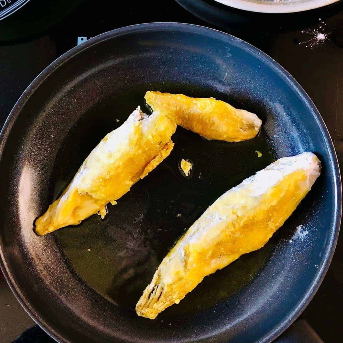 A pan containing three potato starch coated banana blossom frying in a mustard oil