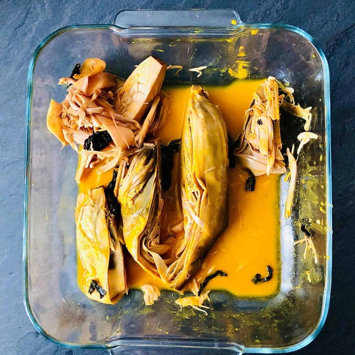 Square glass bowl containing banana blossom marinating in a turmeric, wakame, lemon juice, karla namak marinate.