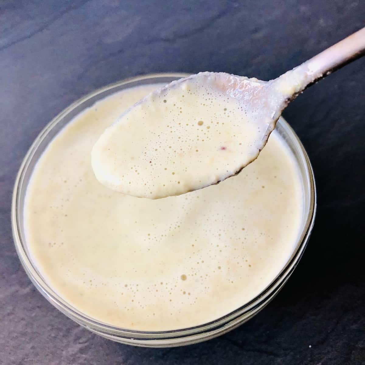 Small glass bowl containing mustard sauce mix. A spoon containing some of the mix is held above the bowl