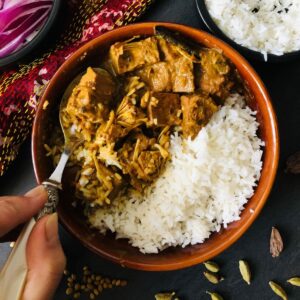 A shallow bowl containing kosha mangsho style vegan jackfruit with plain rice. A hand holds a spoon on the dish.