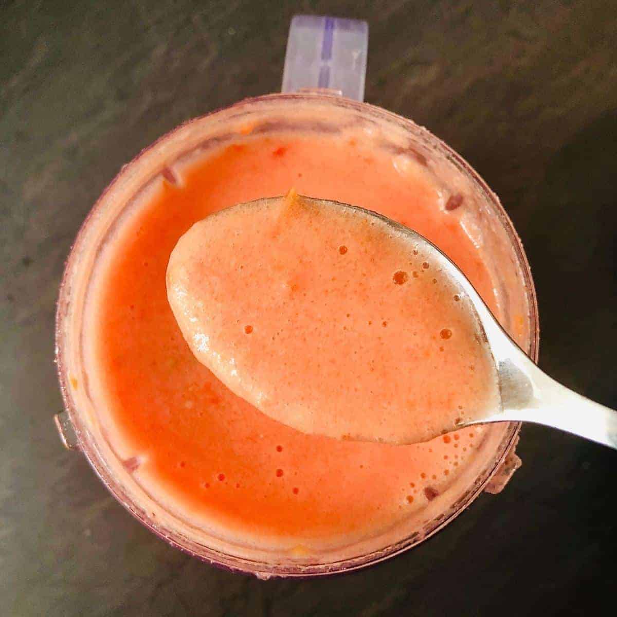 Tomato puree in a spoon held over a blender cup containing the tomato puree