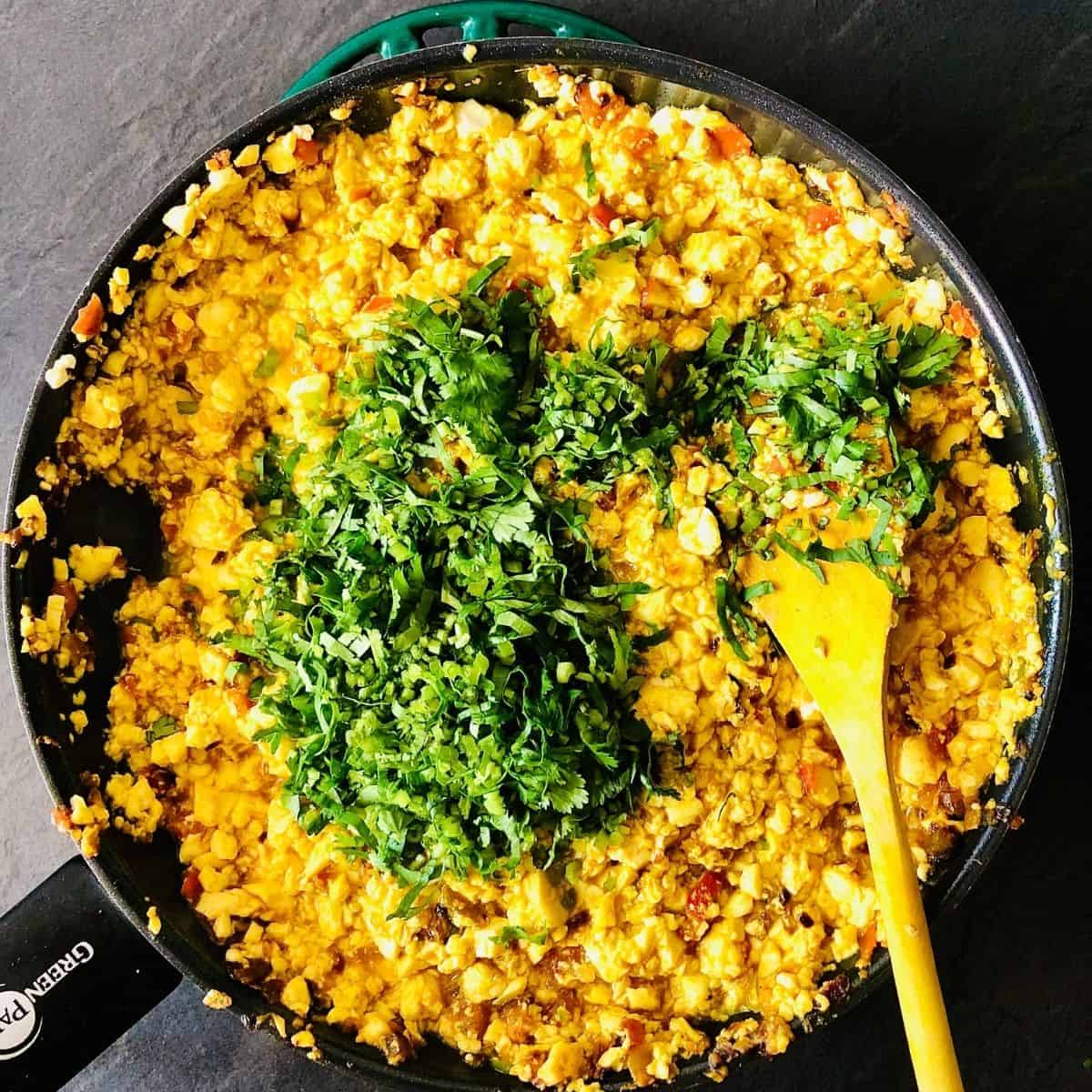 Adding chopped coriander to a frying pan containing scrambled tofu