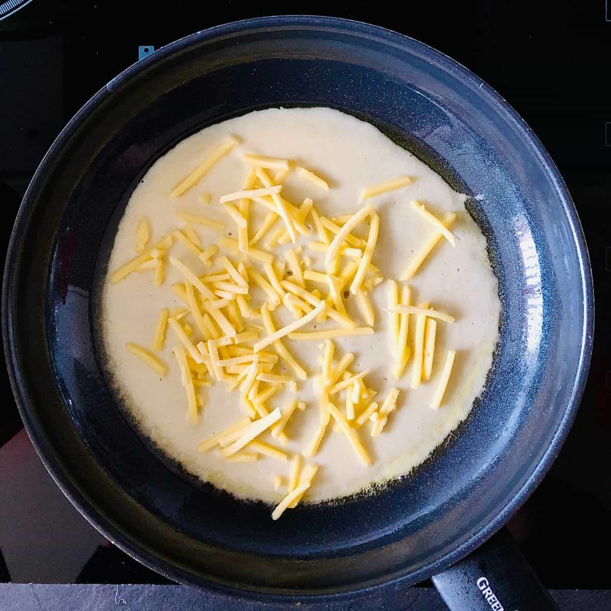 Vegan omelette batter in a frying pan with grated vegan cheese added