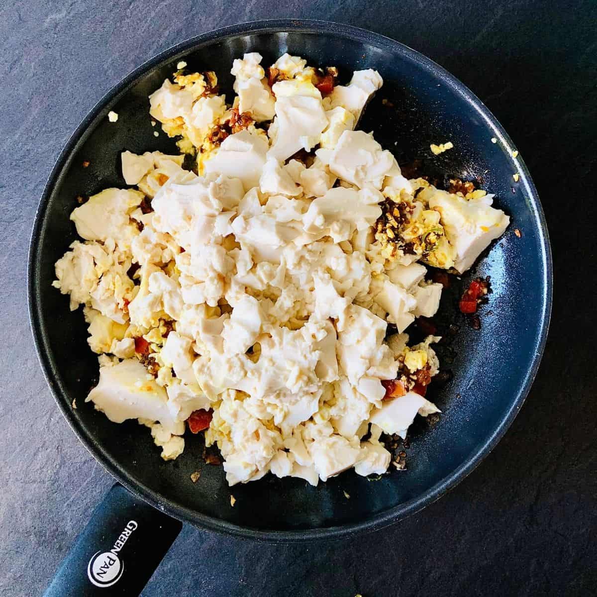 Crumbled tofu added to frying pan containing other cooked ingredients for scrambled tofu