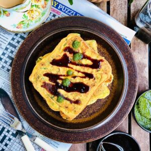 Bread pakora topped with chutney on a brown plate