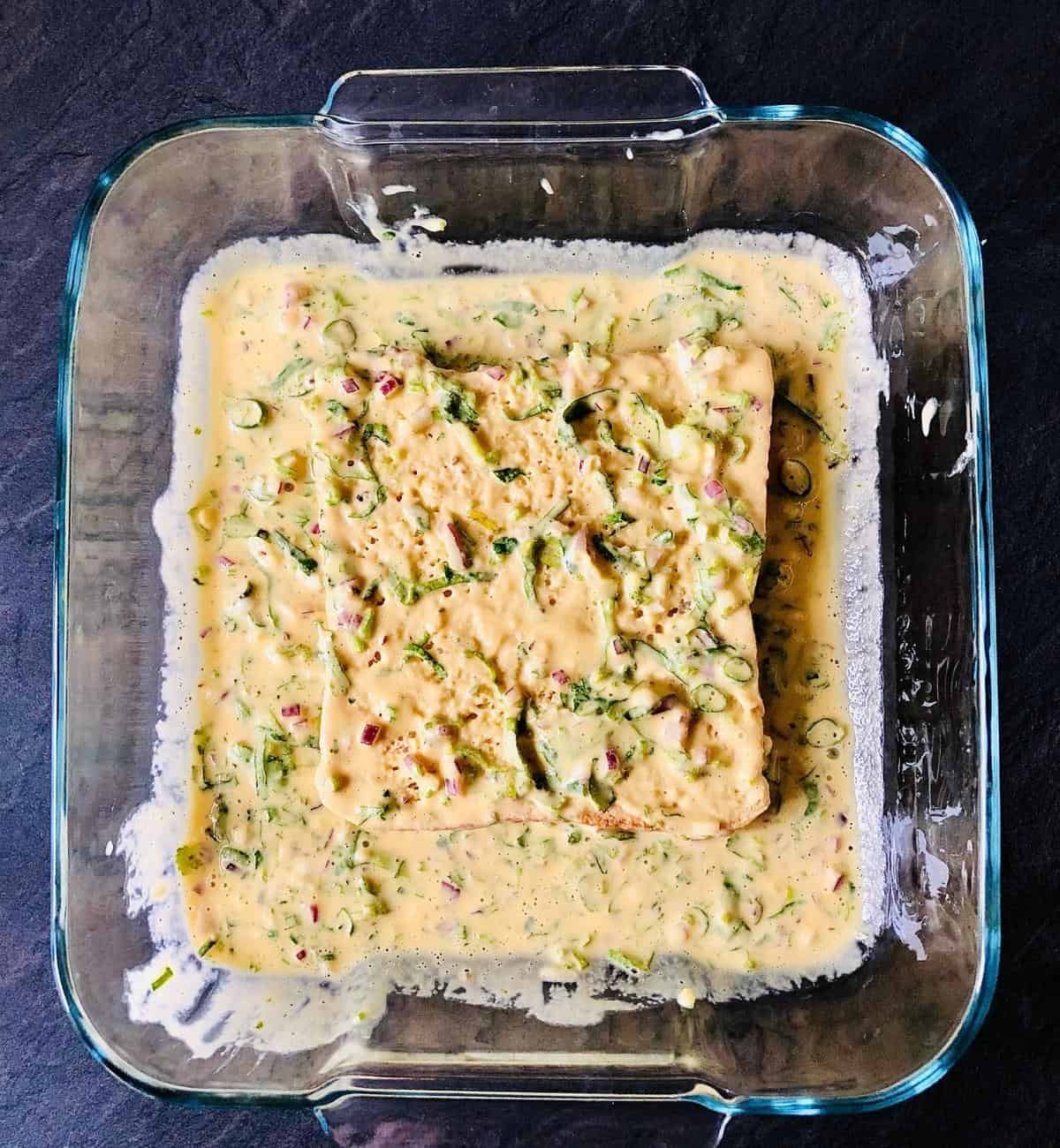 Bread slice coated in gram flour batter for bread pakora. In a glass dish.