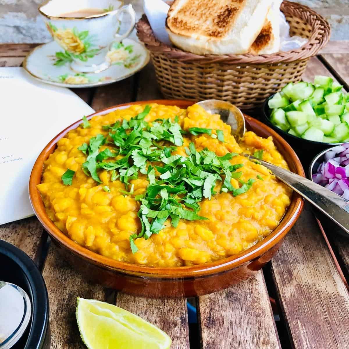 Ghugni mashed white peas garnished with herbs, in a shallow brown dish.