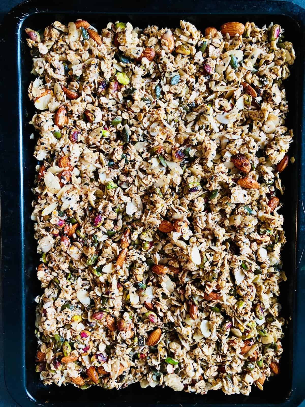 Orange blossom granola spread out on a baking tray ready to cook