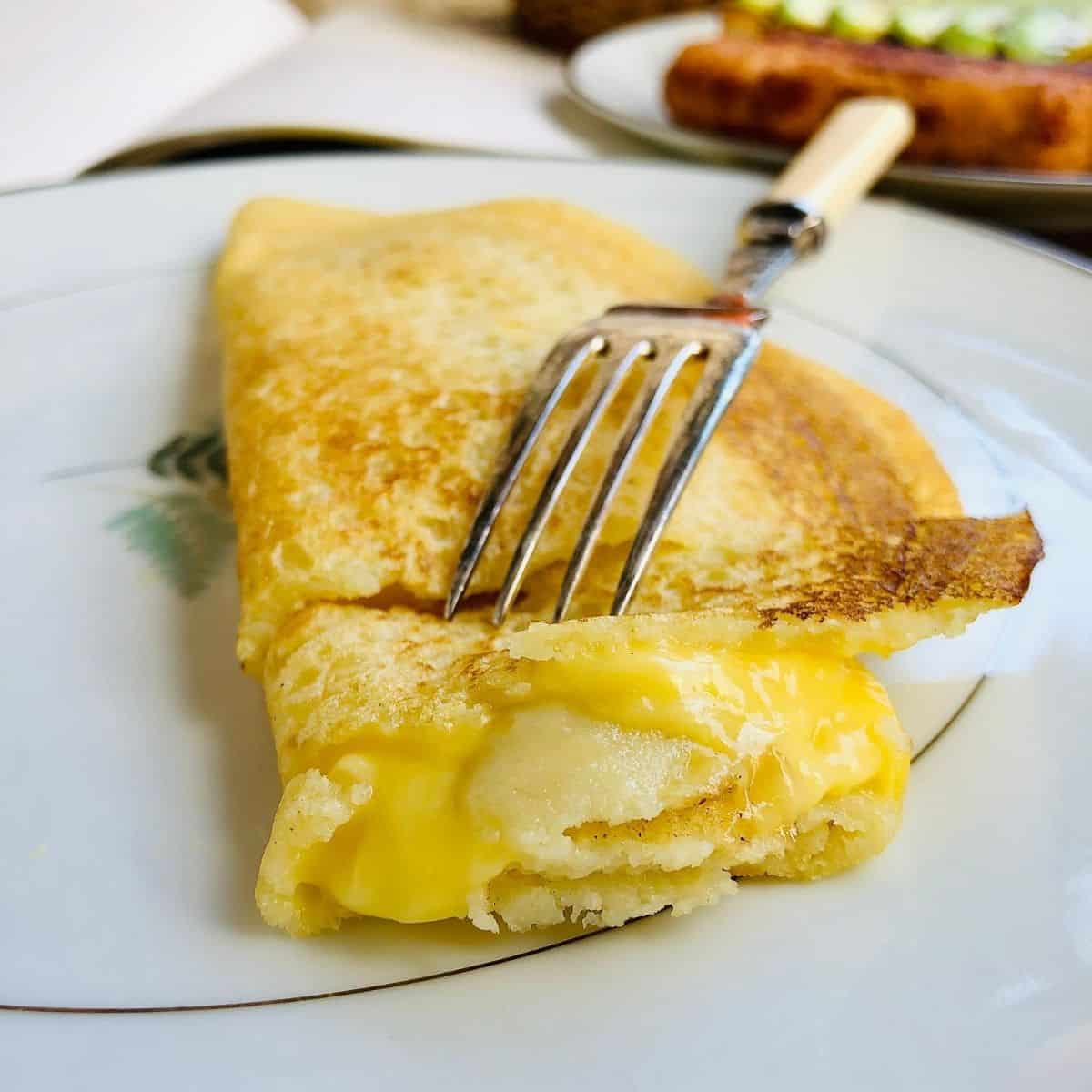 Close up of a vegan omelette on a plate with end cut showing melted vegan cheese filling.