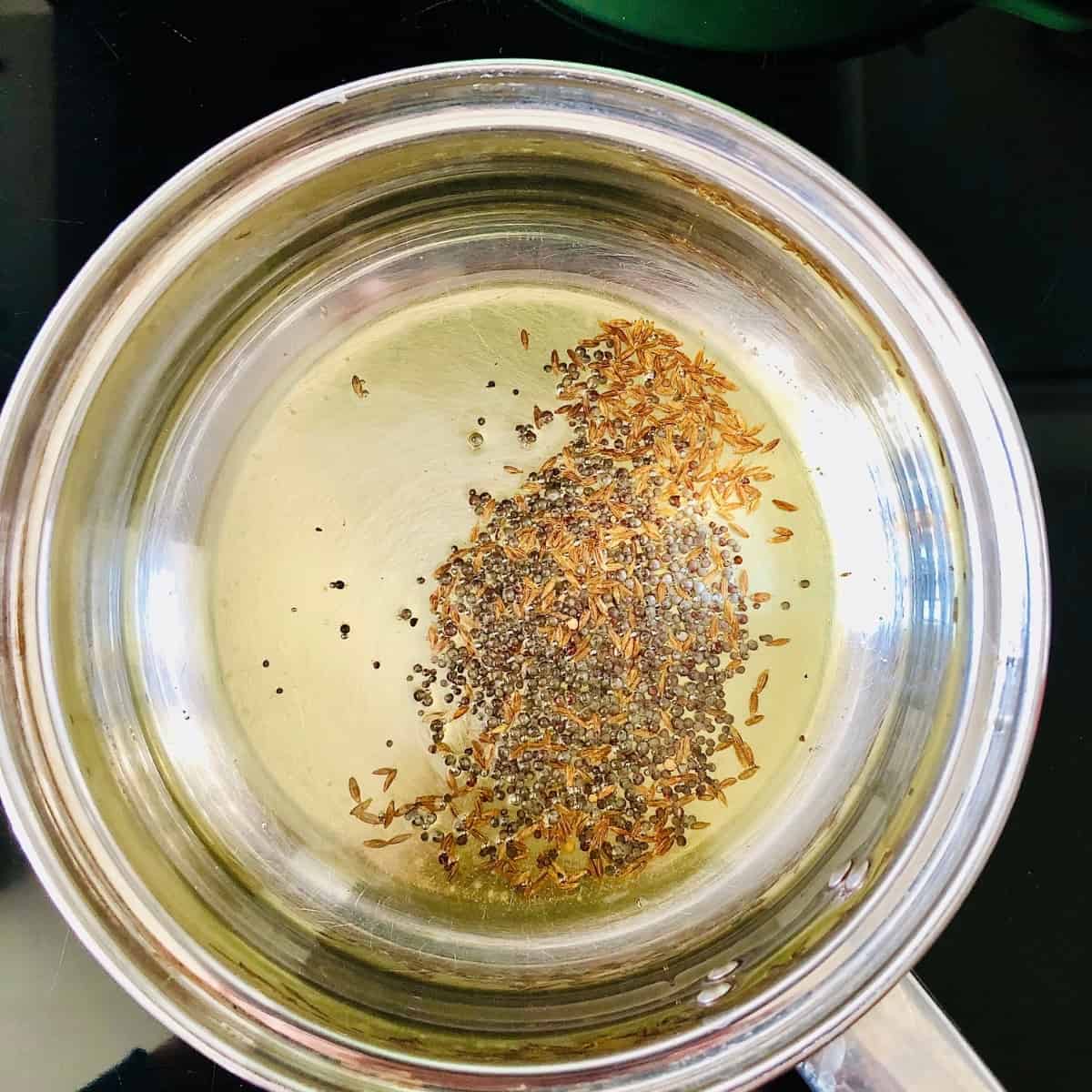 blooming cumin seeds and black mustard seeds in a saucepan for dalia upma healthy breakfast