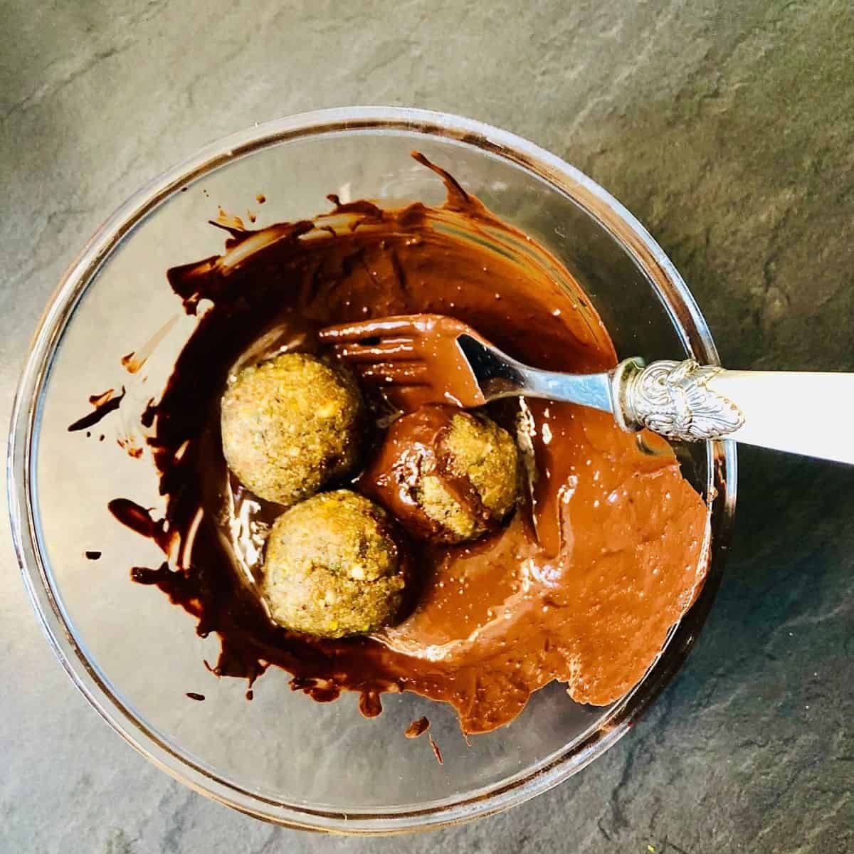 Covering thundai balls in melted chocolate in a glass bowl