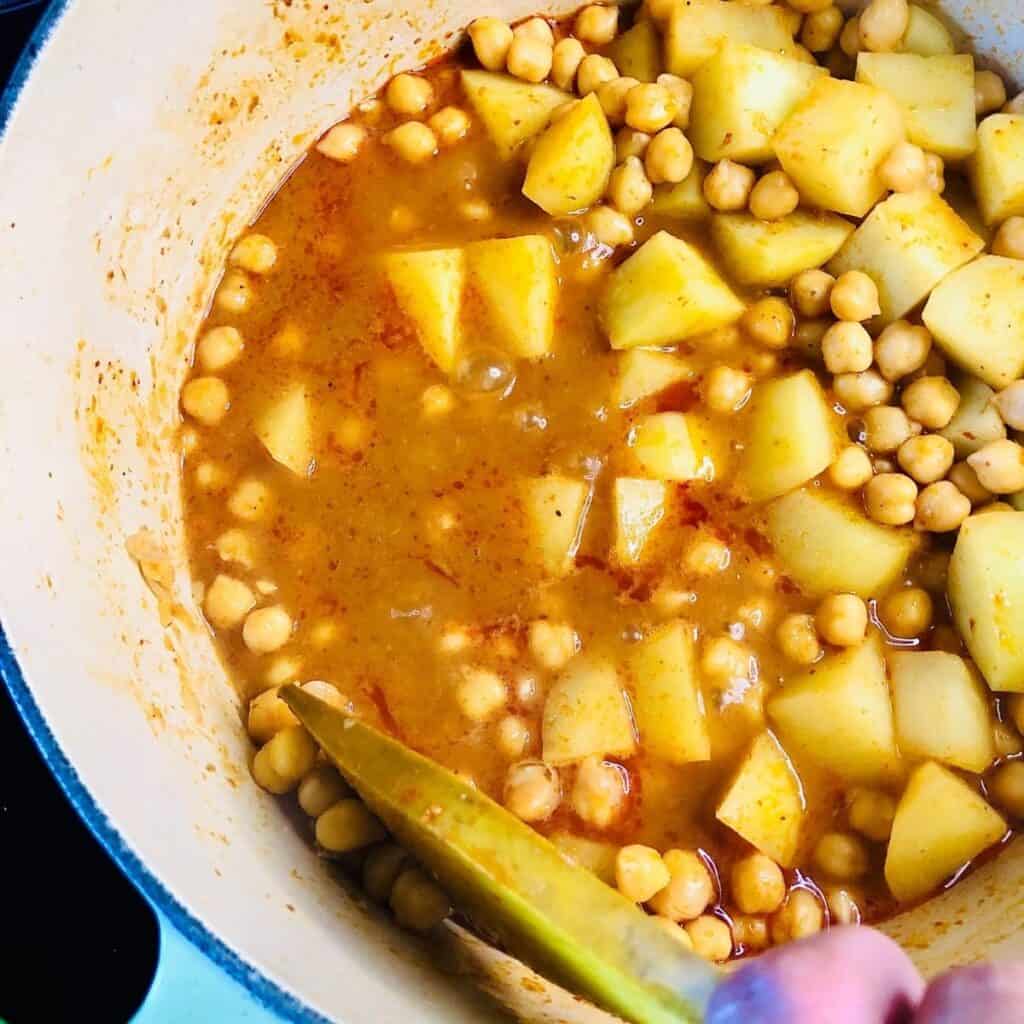 Close up of crushing cooked chickpeas against the side of a pot with a flat wooden spoon