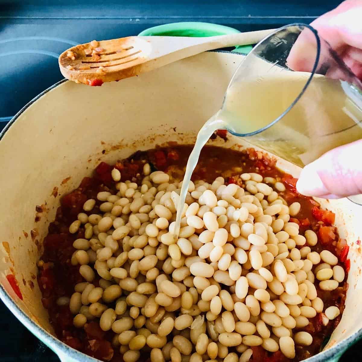 Adding water and beans to the smoky bean mix in a large pot