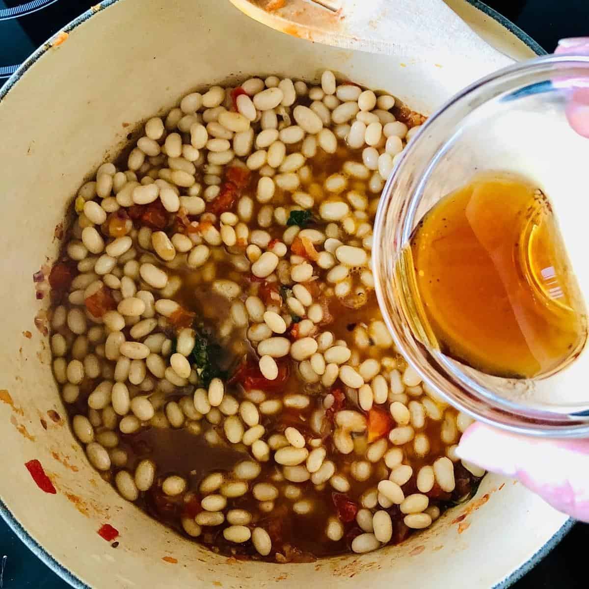 Adding maple syrup to the smoky bean mix in a large pot