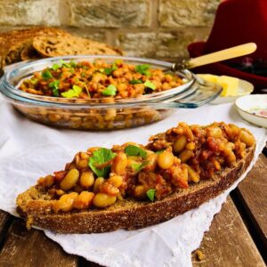 Smoky beans on a slice of sourdough. A dish full of smoky beans sits in the background