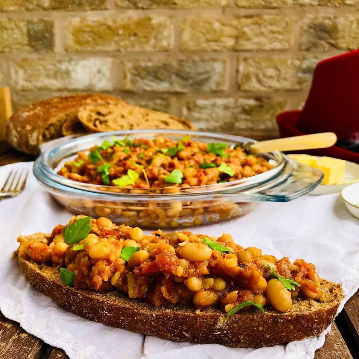 Smoky beans on a slice of sourdough. A dish full of smoky beans sits in the background