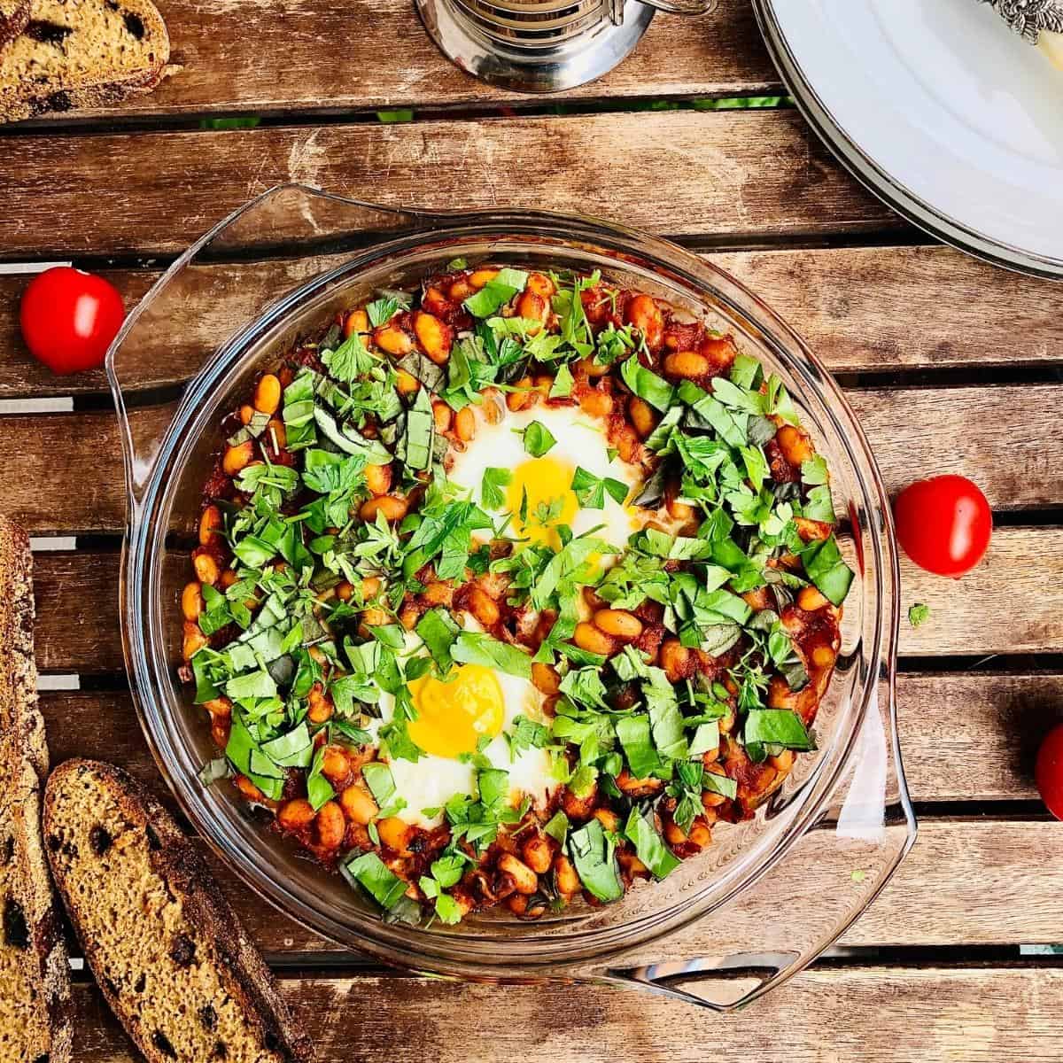 Smoky beans with two eggs garnished with herbs in a shallow glass dish