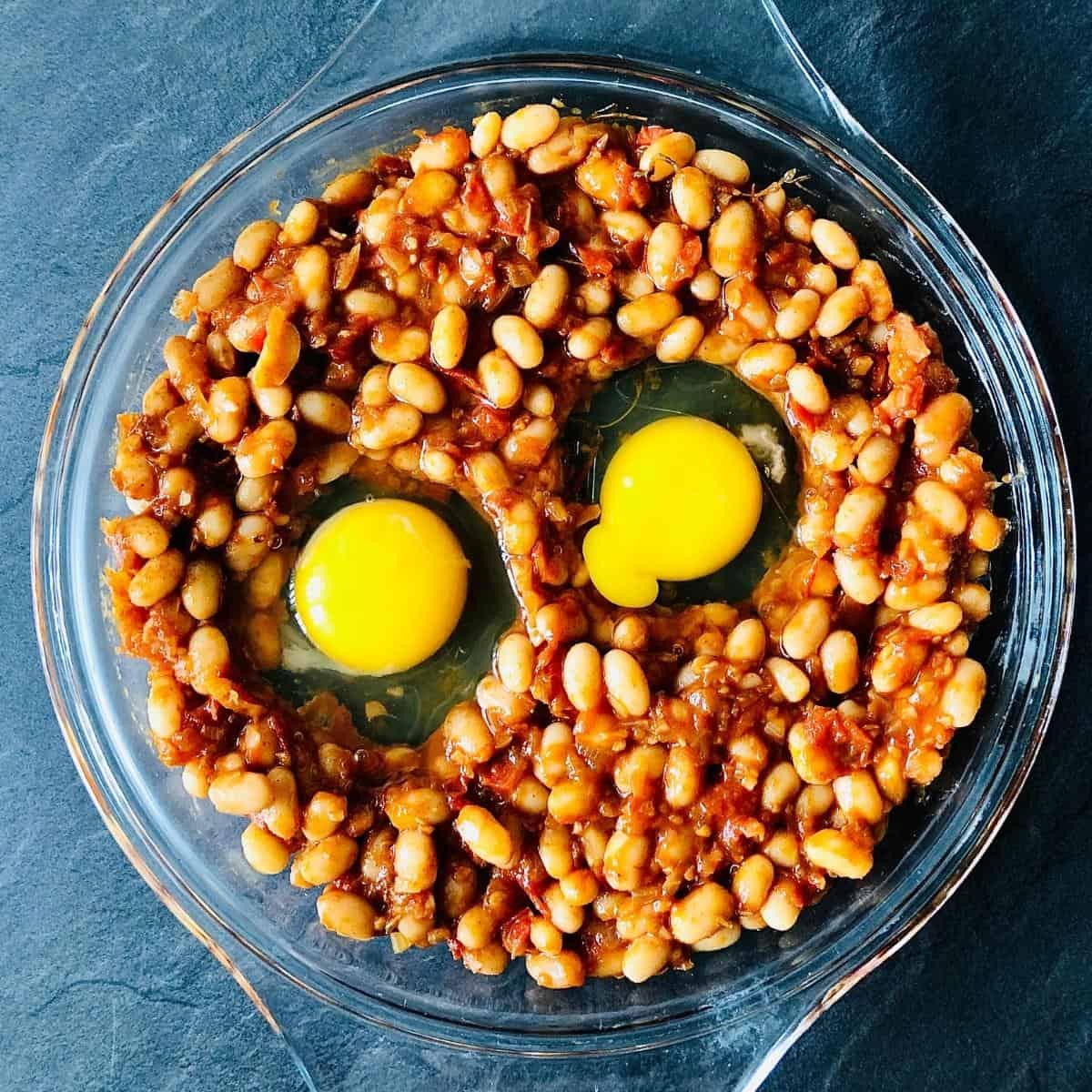 Smoky beans with two uncooked eggs in a shallow glass dish