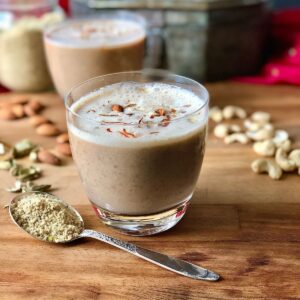 A glass of thandai drink with a teaspoon of thandai powder next to it