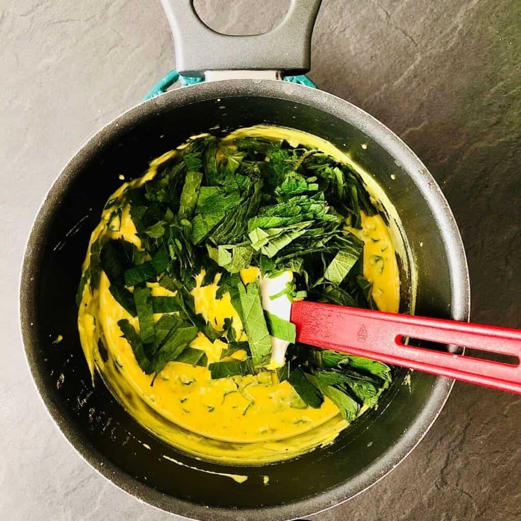 Adding greens to kadhi mixture in a saucepan