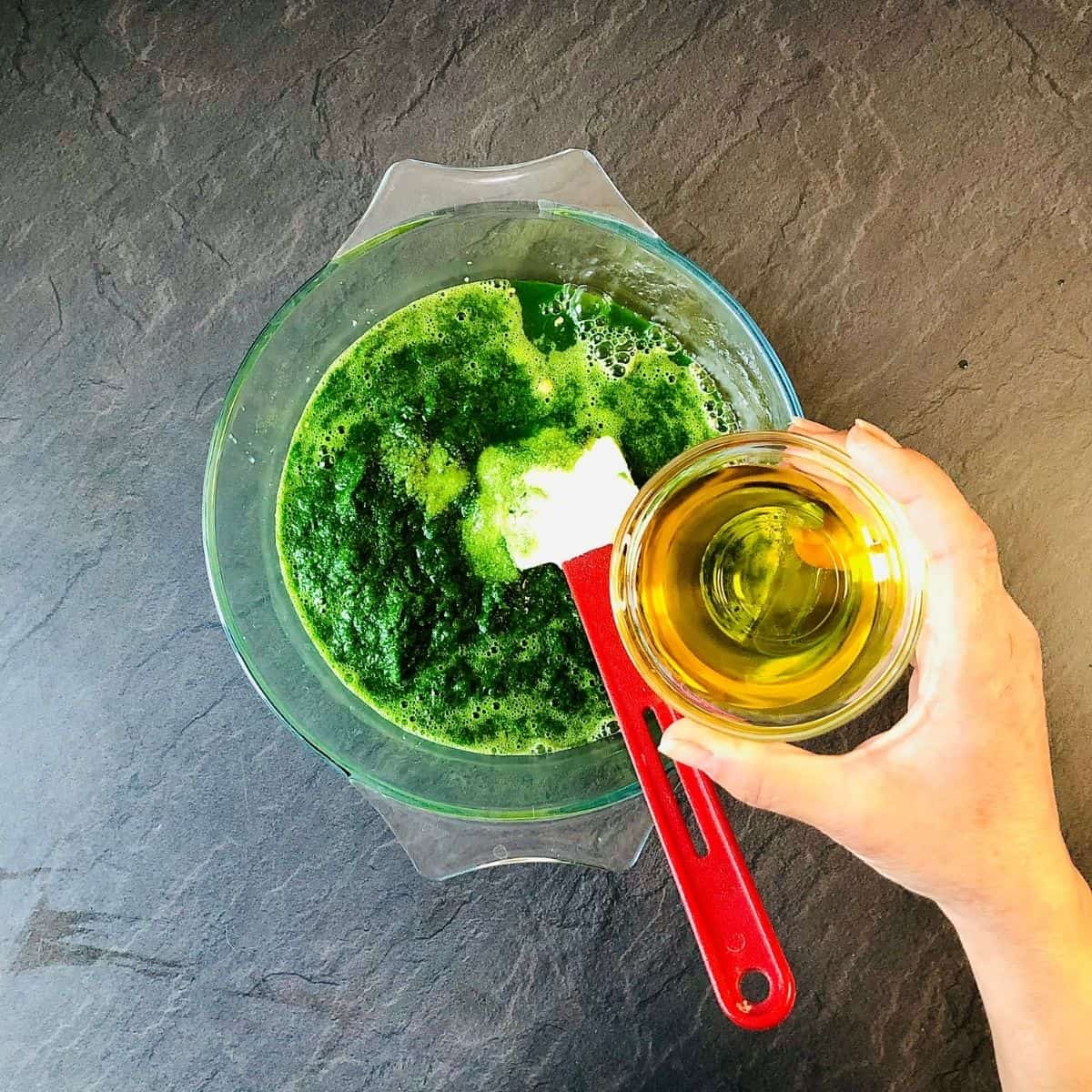 Adding olive oil to a glass bowl containing yeast, caster sugar, and wild garlic puree mixture