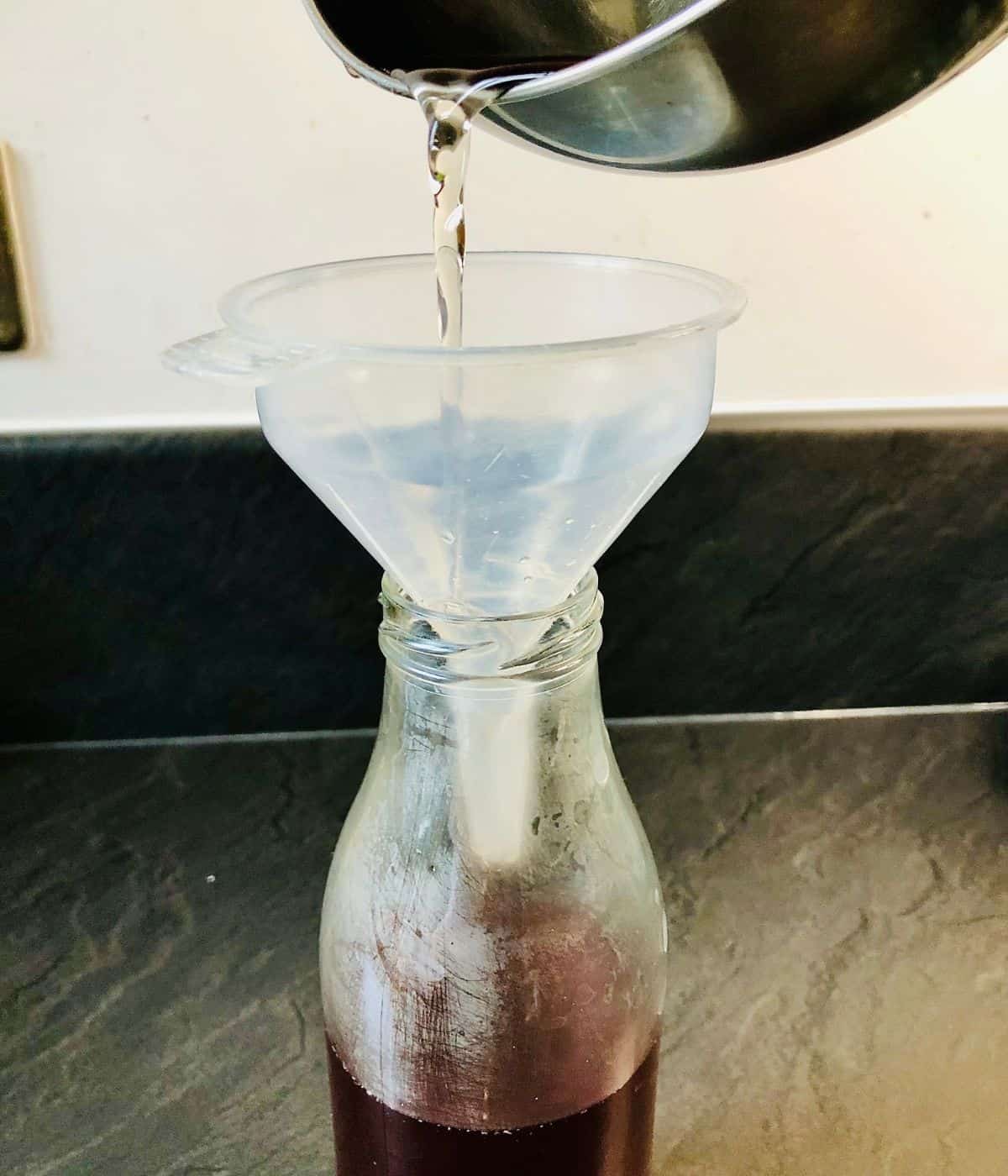 Decanting flowering current cordial into a bottle using a plastic funnel.