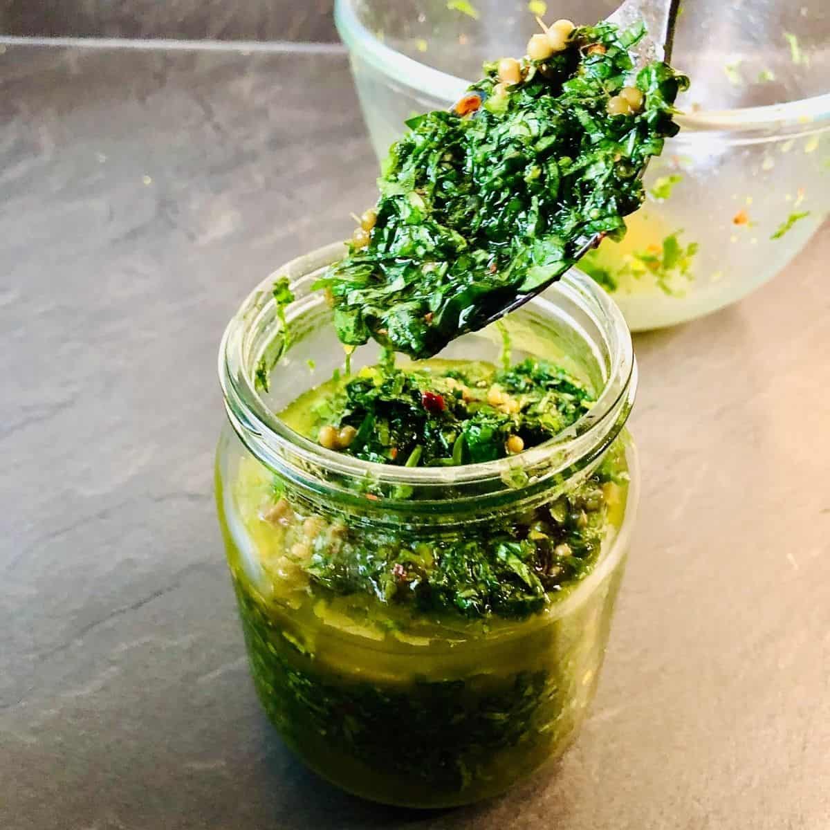 Adding finished salsa verde with wild greens to a jar with a spoon