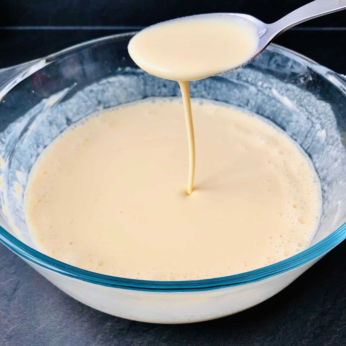 Gram four and vegan yoghurt batter in a glass bowl, thinned with water. Batter is pouring of a spoon