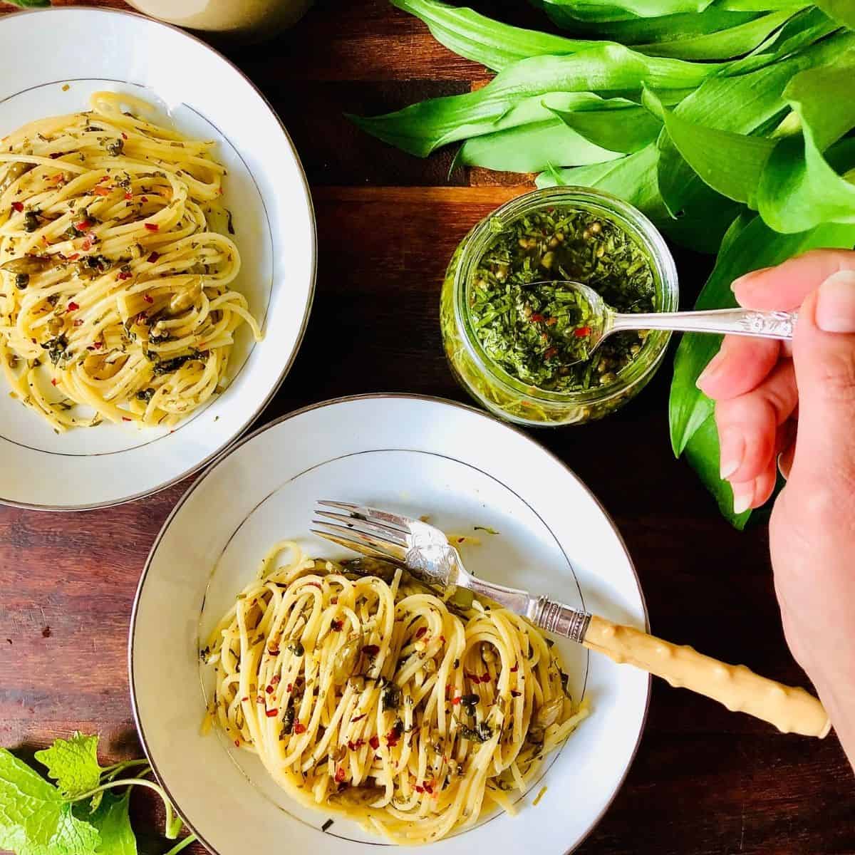 Plate of spaghetti with wild green salsa verde and a jar of wild green salsa verde