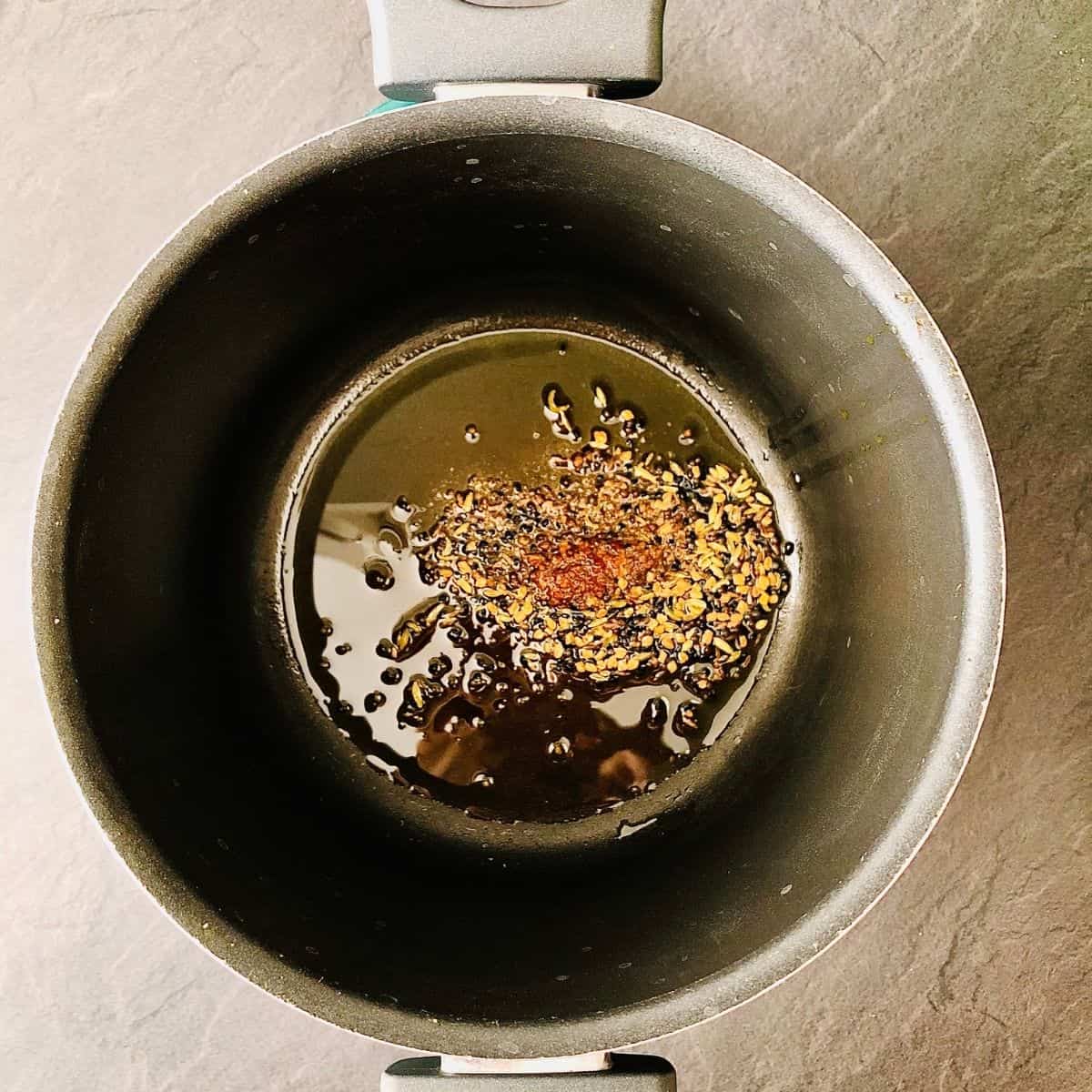 A saucepan containing panchphoran and Asafoetida tempering in hot mustard oil