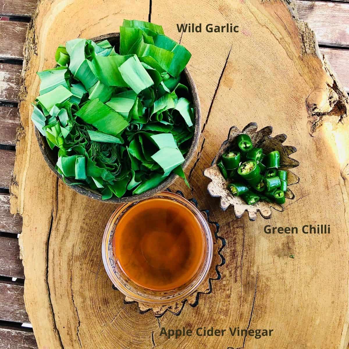 Wild garlic chilli sauce ingredients in small dishes on a wooden tree trunk slice platter