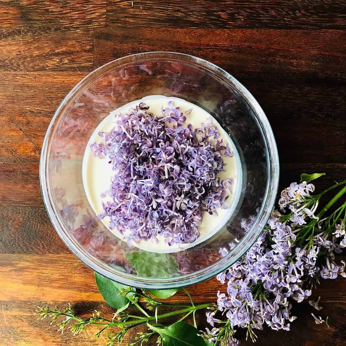 A glass bowl containing vegan whipping cream and lilac flowers for vegan nice cream