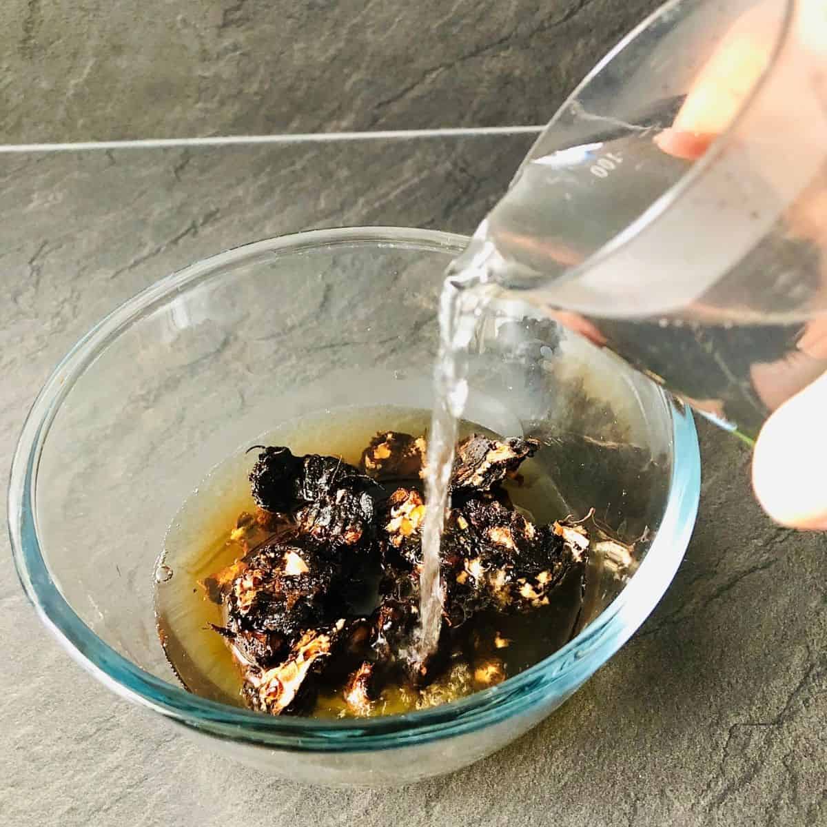 Boiling water pouring into a glass bowl containing dried tamarind