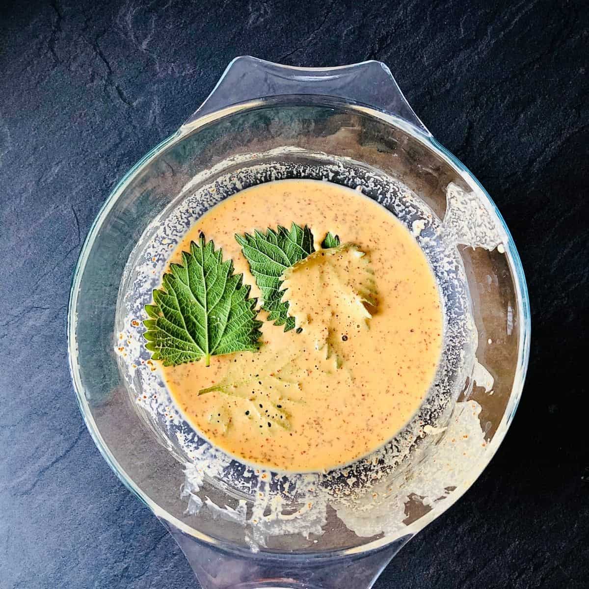 A glass bowl containing Patte Ki Chaat batter with nettles leaves coated in batter