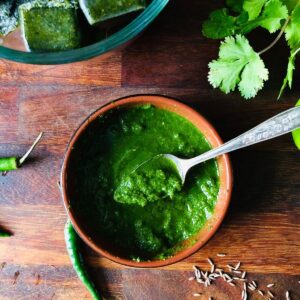 Coriander and cilli chutney in in a shallow dish with a teaspoon.