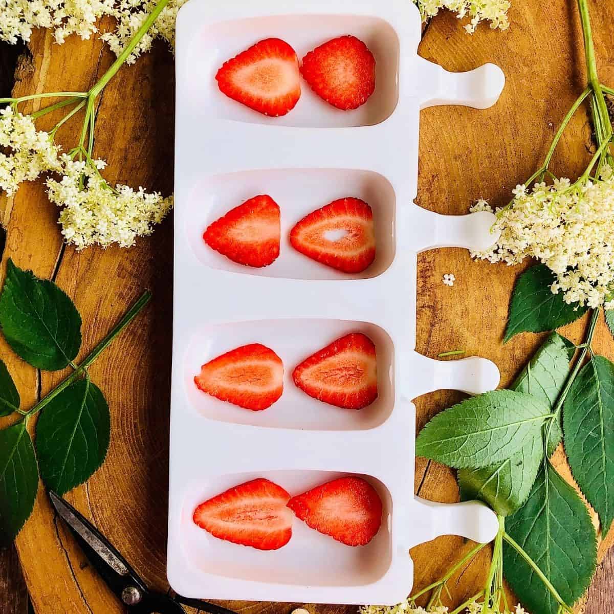 Ice lolly mold with four compartments containing thinly sliced strawberry