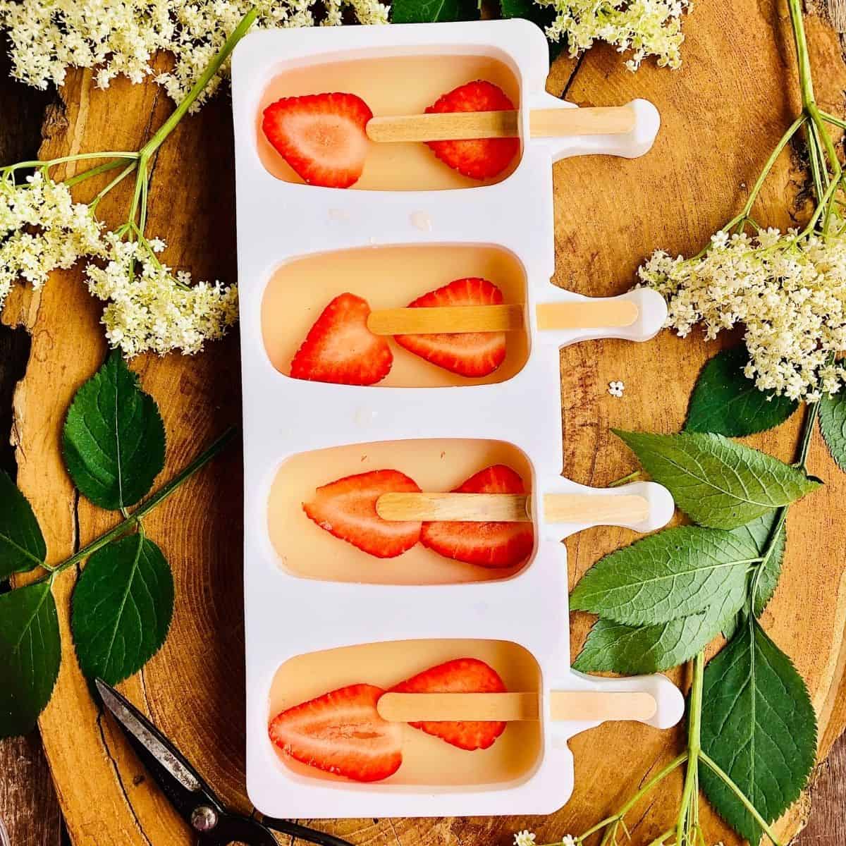 Ice lolly mould containing sliced strawberries and elderflower cordial with lolly stick inserted