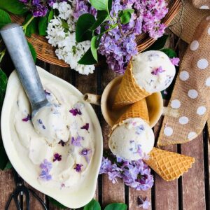 A shallow dish containing lilac nice cream, and two cones with nice cream sat in a stoneware cup next to the dish.