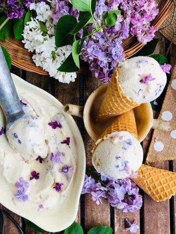 A shallow dish containing lilac nice cream, and two cones with nice cream sat in a stoneware cup next to the dish.