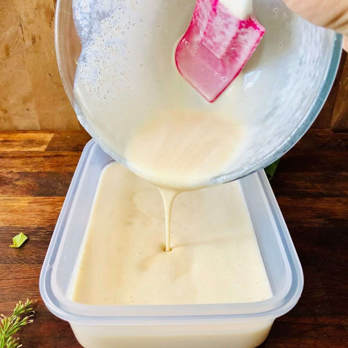 Pouring nice cream mix from a glass bowl into a plastic container