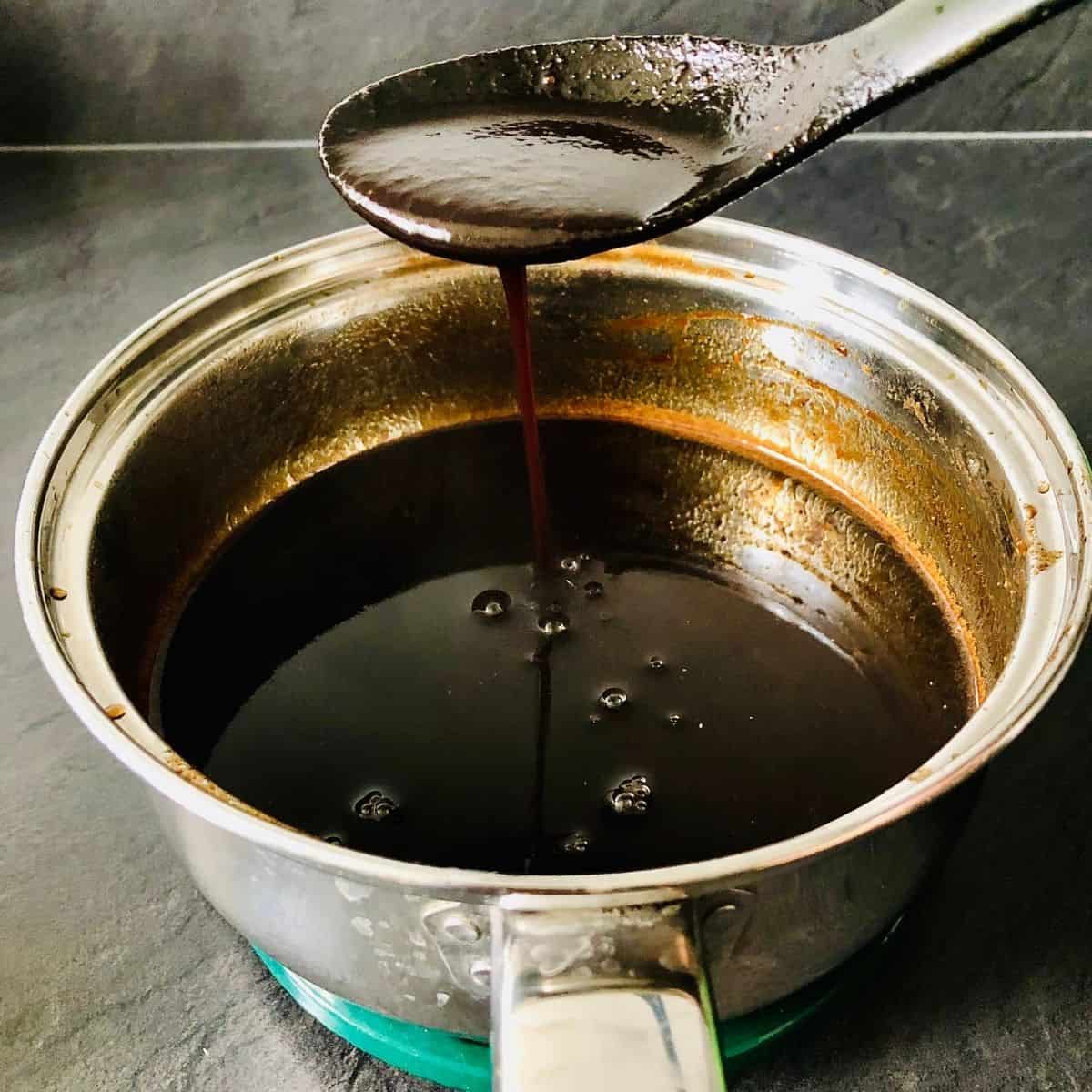 Reduced tamarind syrup pouring off a large spoon into a saucepan containing tamarind syrup