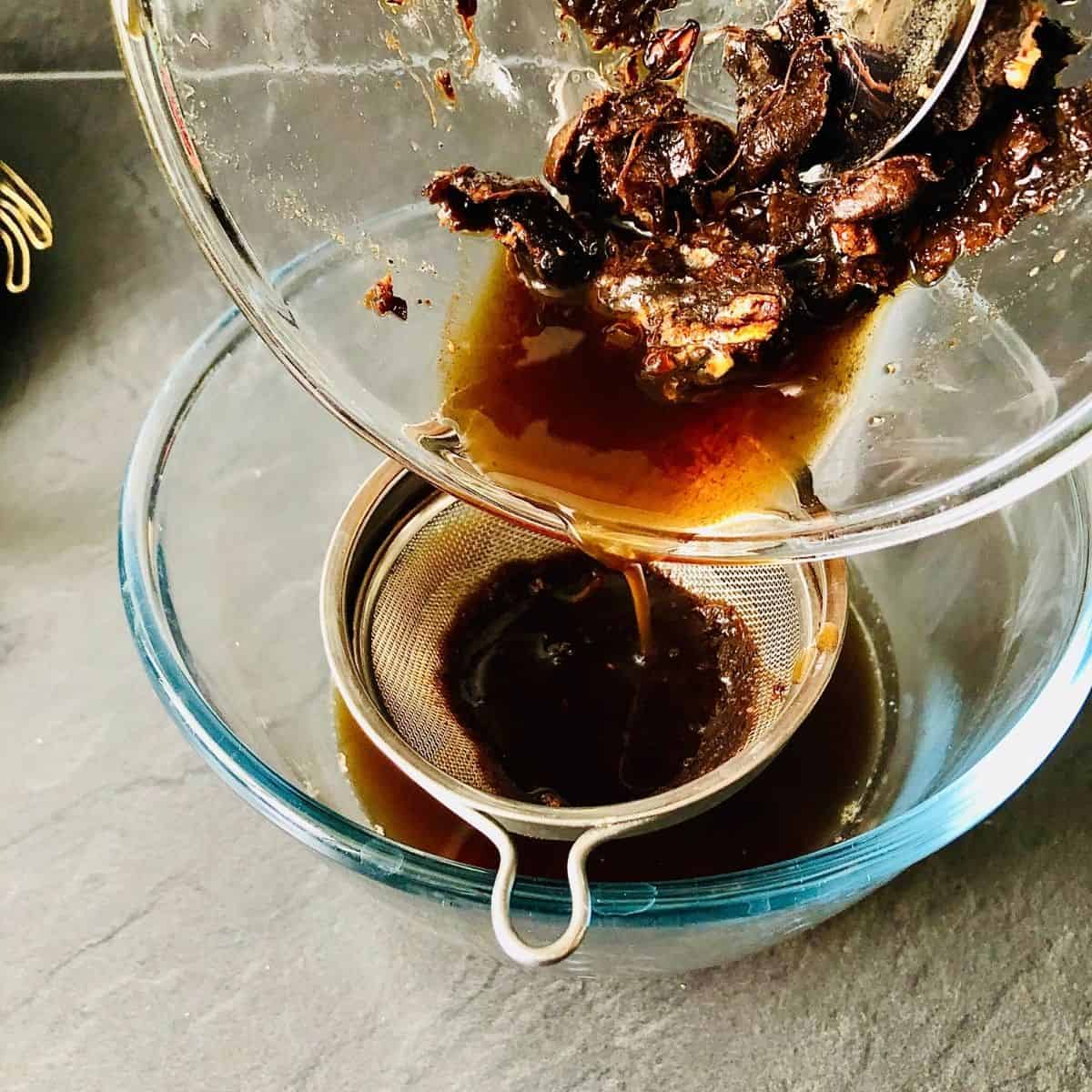 Straining soaked tamarin through a small sieve into a glass bowl.