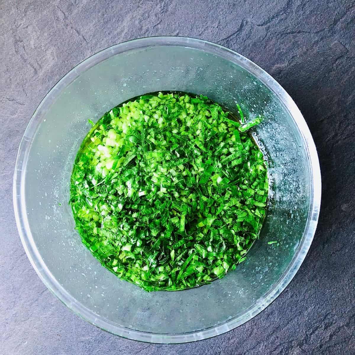 A glass bowl containing wild garlic chilli oil ingredients after hot oil poured over to cook