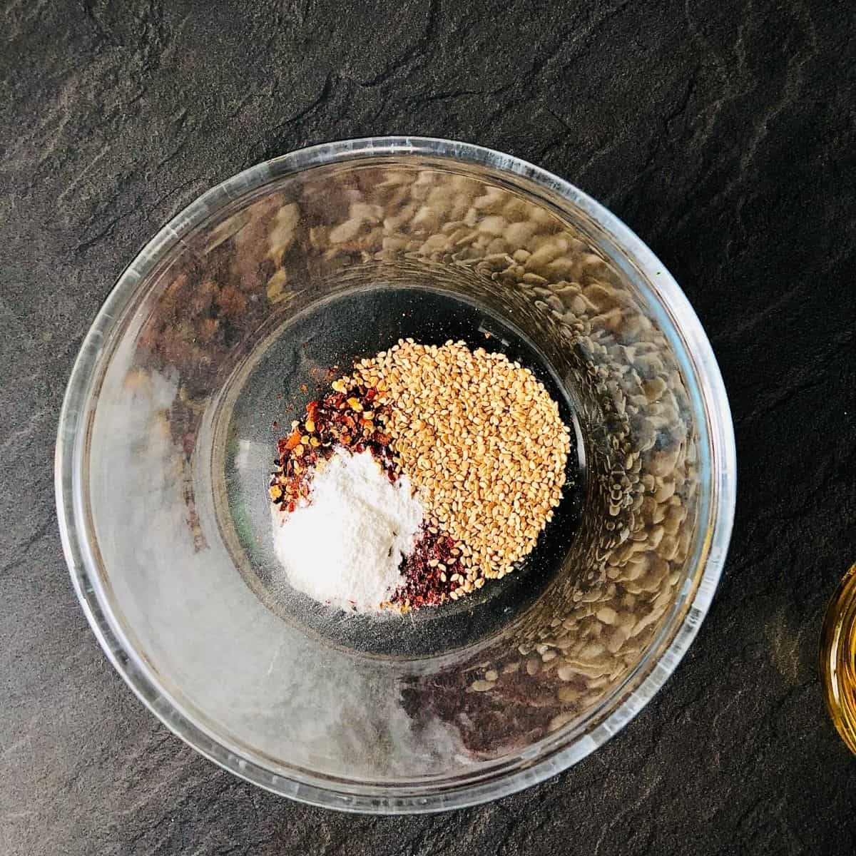 Glass bowl containing chilli flakes, gochugaru, salt and sesame seeds for wild garlic chilli oil