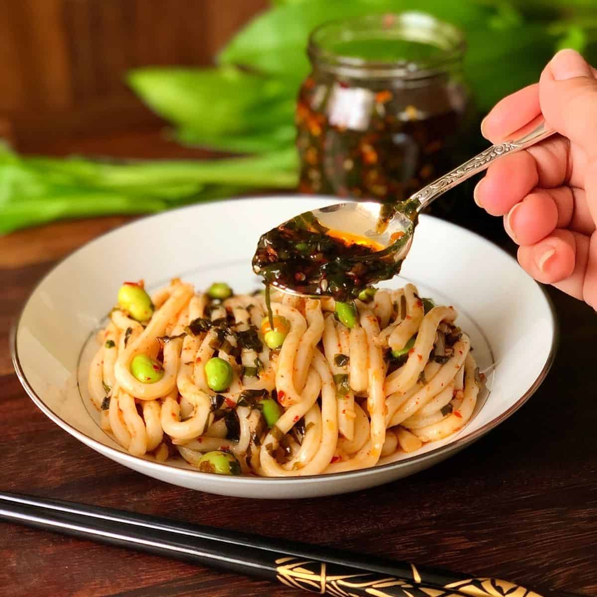 Pouring wild garlic chilli oil with a spoon over noodles in a bowl.