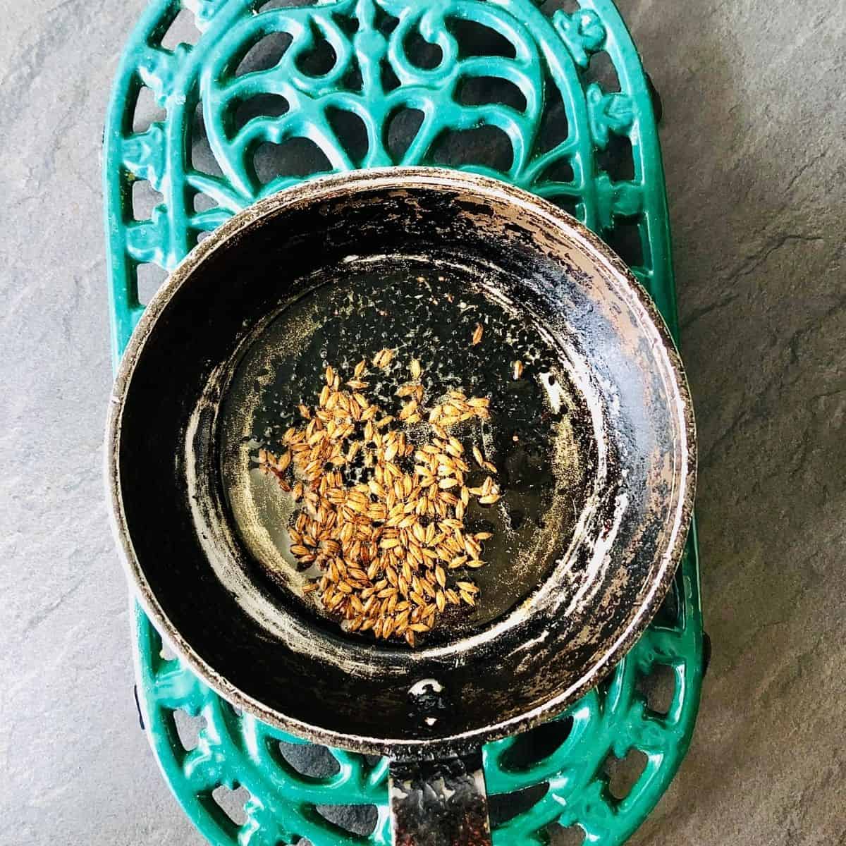 A small frying pan containing bloomed cumin seeds and nigella seeds