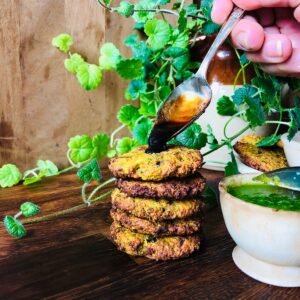 A stack of five broccoli fritters and a teaspoon pouring chutney onto the top fritter.