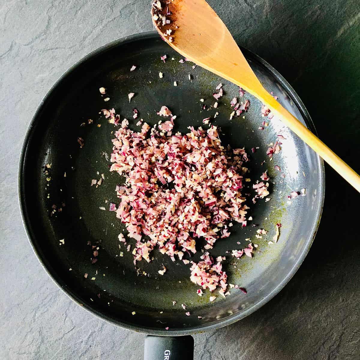 Finely chopped red onion, garlic and ginger cooking in a frying pan