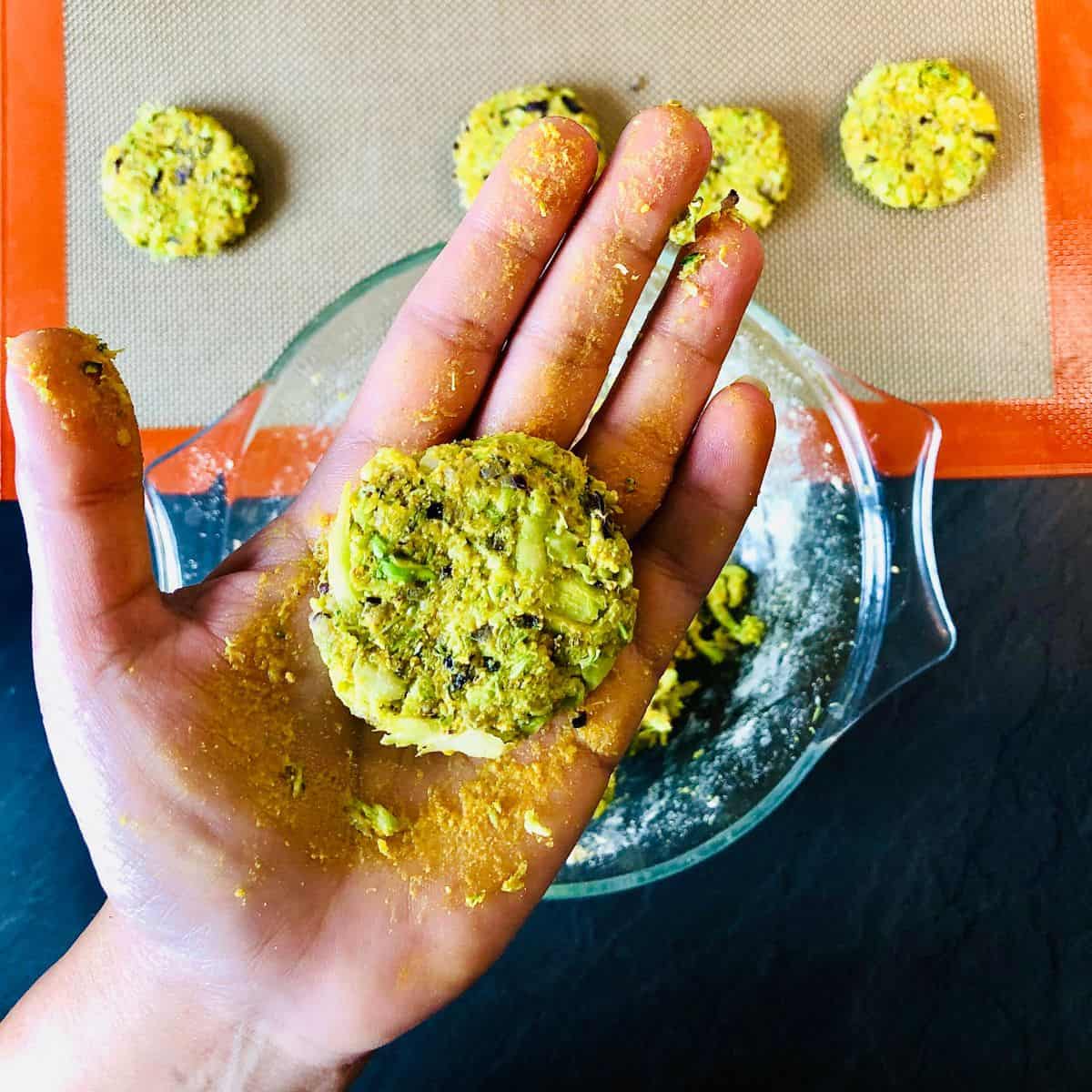 Close up of an uncooked broccoli fritter held in the palm of a hand.
